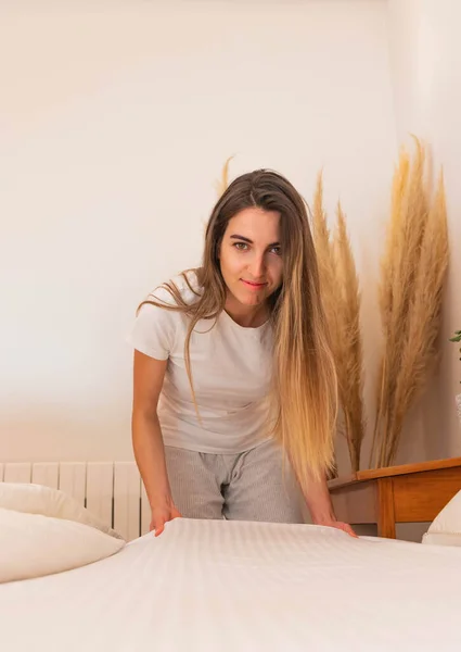 Young woman crouching looking at the camera stretching the sheets of the bed early in the morning