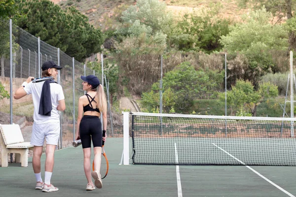 Back view of two friends walking through a tennis court about to play a friendly tennis match to be in shape — Stock fotografie
