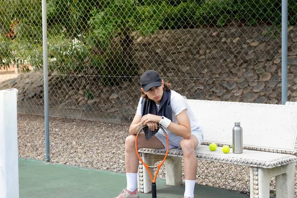 Joven tenista sentado derrotado en un partido de tenis. Muy cansado y con una cara desilusionada en una pista de tenis — Foto de Stock