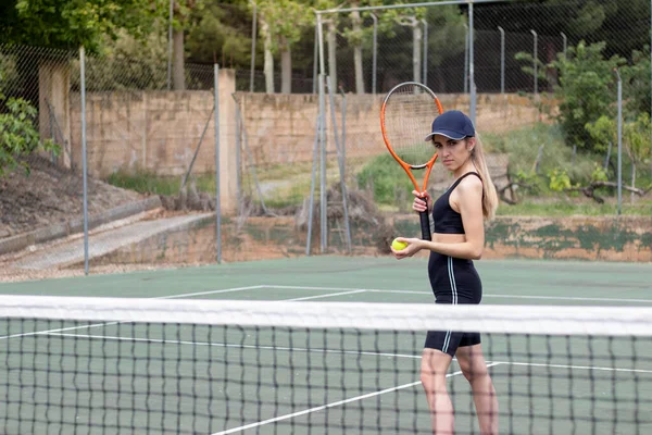 Nézet a fiatal gyönyörű nő, aki a kamera kész játszani egy tenisz mérkőzés a zöld udvaron — Stock Fotó