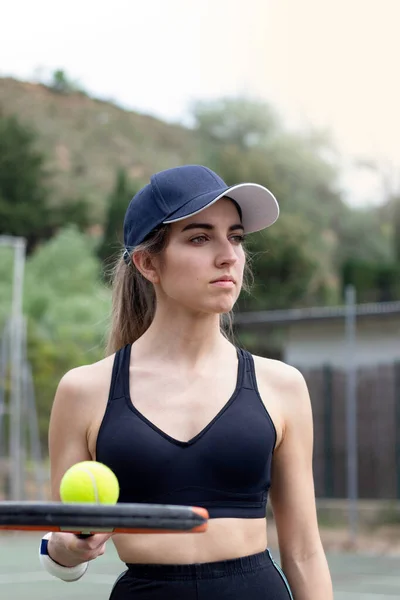 Függőleges portré fiatal nő teniszező nézi az oldalán kezében egy ütő és egy labda visel fekete ruhát — Stock Fotó