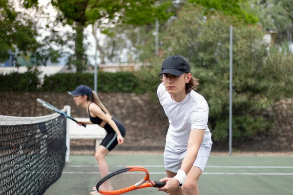 Boční pohled na muže a ženy tenis pár soustředí na hraní zápas v blízkosti sítě se snaží trefit míč. — Stock fotografie