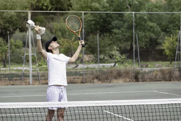 Professional man tennis player enjoying his victory with a cup in hand. Looking up at the sky and raising the arms