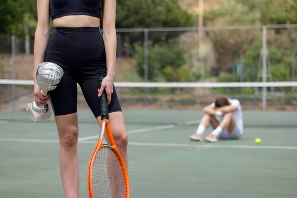 Female winner of the tennis tournament with cup in hand on the front and looser man on the background out of focus — Stock Photo, Image