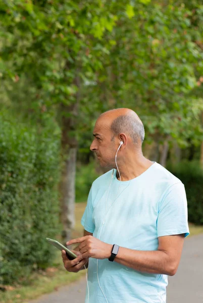 Side portrait of a hairless man listening to music with headphones on his cell phone in nature as he walks through the countryside