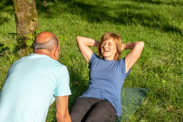 Close up protrait of two older men and woman exercising while having fun in the park with grass and nature in sunny day