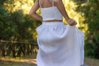 Tanımlanamayan genç bir kadının hareket edişini ve arka planda doğayla iç içe olan uzun, beyaz eteğini nasıl tuttuğunu.