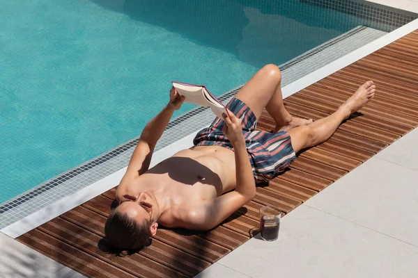 Jongeman Het Zwembad Een Boek Lezen Een Cola Drinken Onder — Stockfoto