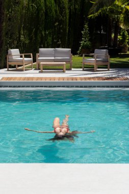 Vertical view of young woman in bikini relaxing upside down floating in the middle of the swimming pool in summer