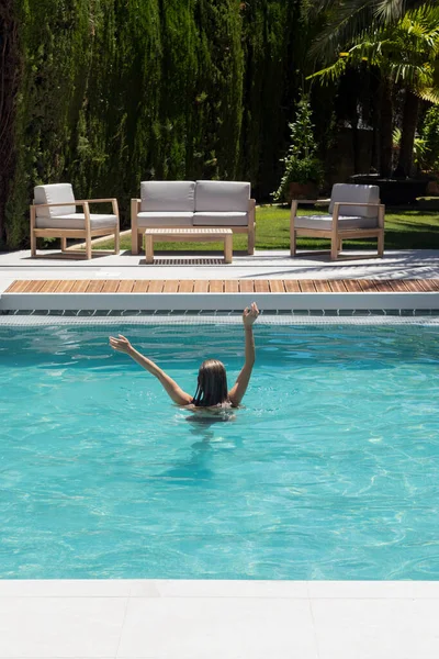 Vertical view of young unrecognizabel woman enjoying the refreshing time in the swimming pool in hot summer day in the garden