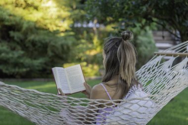 Kamp hamağında kitap okuyan tanınmayan bir kadının yaz aylarında eğlence amaçlı kitap okuması.