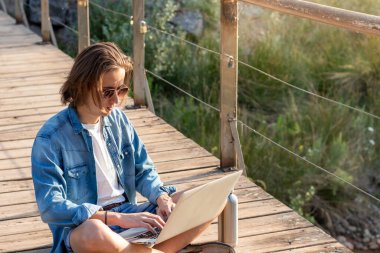 İnternette uzun saçlı serbest çalışan genç bir adamın portresi. Tatildeyken dizüstü bilgisayarında sallanıyor.