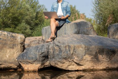 Dizüstü bilgisayarıyla çalışan genç bir adamın tanınmaz halde portresi İspanya 'da bir nehrin kenarında kırmızı bir tablonun üzerinde oturuyor.