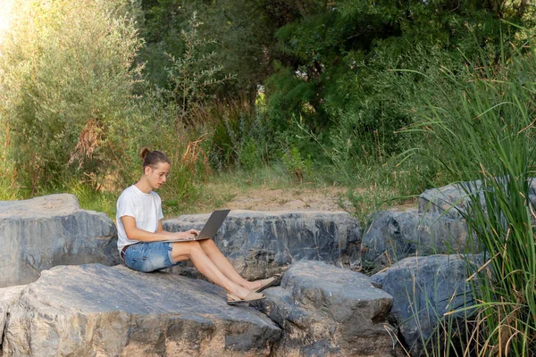 Doğada dolaşırken bilgisayarıyla çalışan genç bir erkeğin yan portresi.