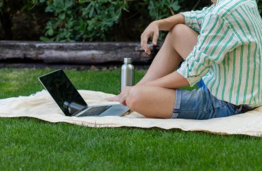 Yazın boş zamanlarında bahçede oturup bilgisayarı kullanan tanınmamış genç bir adam.
