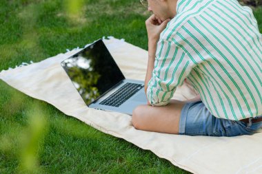 Baharda bir ağacın altında duran bilgisayarı kullanarak konsantre olan yüzü olmayan genç adamın arka görüntüsü.