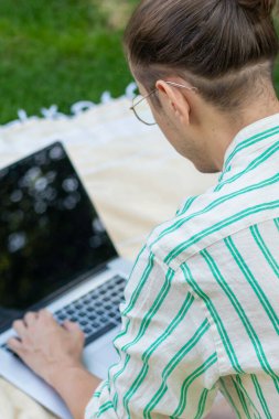 Dikey arka plan. Baharda ev bahçesinde dizüstü bilgisayarda çalışan bir adamın seçici odak noktası.