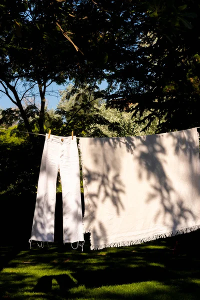 Hanging out pants an linen clothes in a clothes line in the garden with plant shadow on them and natural boho style