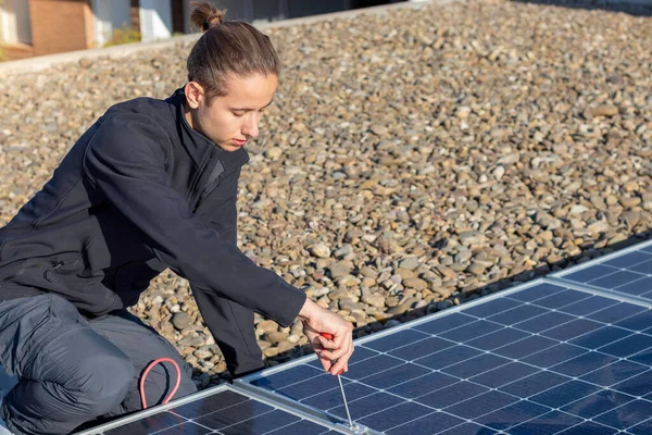 Concentrated young man worker with bun hairstyle screwing and assembling new solar apnels for eco solar energy source