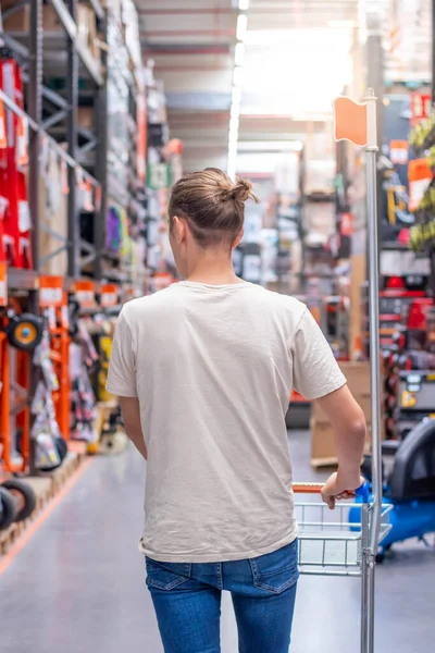 Vertical view of young man from the back carrying a trolley in the hallway of a hardware store warehouse