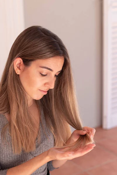 Vertical view of young blond woman looking concerned her damage hair on her hand