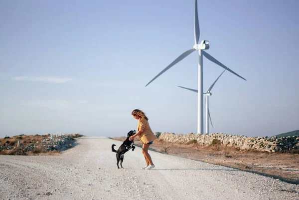Arka planda rüzgar türbinleri olan bir köpekle tarlada yürüyen kadınlar.