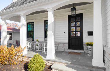 OAK PARK, IL, ABD - 28 Ekim 2020: Pencereleri, beyaz sütunları, taş zemini ve bahçe mobilyaları olan koyu renkli beyaz ahşap kapılı yeni bir çiftlik evi.