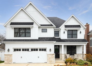 OAK PARK, IL, ABD - 2 Kasım 2020: Koyu kiremitli çatısı ve siyah pencereleri olan yeni, beyaz bir çiftlik evi. Evin altında hafif bir kaya kaplaması ve verandası var..