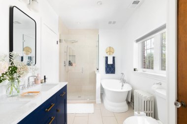 ELMHURST, IL, ABD - 2 Eylül 2021: Mavi makyaj dolabı, fayanslı duşu ve standalone banyo küveti olan güzel yenilenmiş bir banyo.