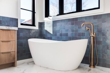 ELMHURST, IL, ABD - 1 Kasım 2020: Beyaz bir ayakta duran küvet ve altın musluğun güzel, lüks banyo detay çekimi beyaz mermer döşemeler ve mavi bir duvarın önünde oturan altın musluk.