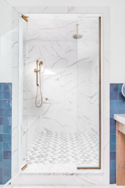 OAK PARK, IL, ABD - 15 Eylül 2020: Mermer döşemeler, cam bir kapı ve altın duş başlığı ile güzel fayanslı bir duşun kapısına bakıyorum. Banyo mavi kiremitlerle kaplı..
