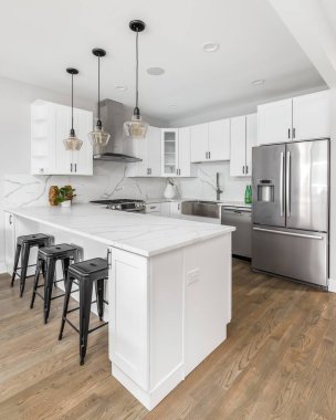 Şikago, IL, ABD - 22 Ocak 2020: Tavandan sarkan siyah ışıklar ve yemek odası tezgahında duran siyah bar tabureleri ile modern, tamamen beyaz bir mutfak. Işıkları kapat..