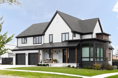 BARRINGTON, IL, ABD - 5 Ekim 2021: Beyaz ve siyah kaplamalı modern bir çiftlik evi, bir ön veranda ve siyah kapılı iki araba garajı.