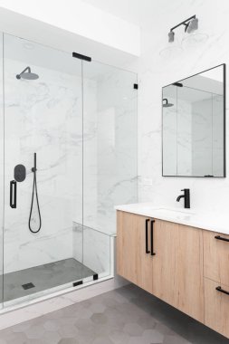 ELMHURST, IL ABD - 28 Haziran 2021: Güzel bir lüks, modern banyo hafif ahşap bir dolabı, mermer döşeme duvarları, siyah muslukları ve donanımlı duşu olan.