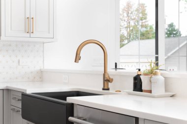 CHICAGO, IL, ABD - 2 Haziran 2021: Altından bir musluk, siyah önlük veya çiftlik evi lavabosu, beyaz granit ve seramik kaplama ile yenilenmiş modern bir çiftlik evi mutfağında güzel bir lavabo.