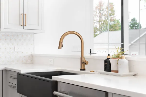 CHICAGO, IL, ABD - 2 Haziran 2021: Altından bir musluk, siyah önlük veya çiftlik evi lavabosu, beyaz granit ve seramik kaplama ile yenilenmiş modern bir çiftlik evi mutfağında güzel bir lavabo.