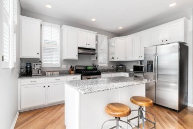 Chicago, IL, ABD - 3 Haziran 2019: Gri mermer tezgahları, paslanmaz çelik aletleri ve adada oturan ahşap koltuk bar tabureleri olan beyaz bir mutfak.