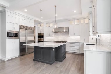 CHICAGO, IL, USA - APRIL 23, 2020: A luxurious modern white kitchen with stainless steel Wolf, Subzero, and Whirlpool appliances. A large island sits in the middle with two fancy lights hanging above. clipart