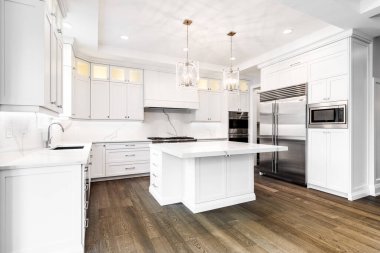 CHICAGO, IL, USA - AUGUST 17, 2019: A luxurious modern white kitchen with stainless steel Wolf, Subzero, and Whirlpool appliances. A large island sits in the middle with two fancy lights hanging. clipart