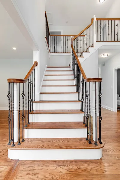 Looking up a household staircase with wrought iron railings, wood banisters, and hardwood floors throughout the house.