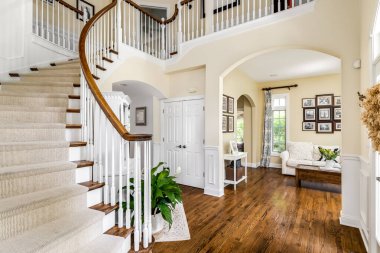 ELMHURST, IL, ABD - 22 Mayıs 2020: Lüks evlerin fuayesinde rahat bir oturma odası, kanepe ve sehpa manzaralı dairesel bir merdiven.
