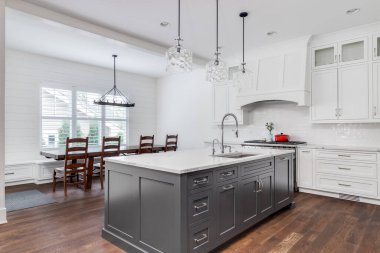 Şikago, IL, ABD - 21 Temmuz 2020: Büyük gri bir adada oturan bar tabureleriyle lüks bir beyaz mutfak ve tavandan sarkan cam lambalar yemek odasına bakıyor.