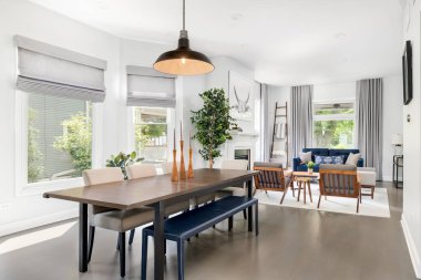 OAK PARK, IL, ABD - 7 AĞUSTOS 2020: Modern bir yemek odası oturma odasına bakıyor. Büyük masanın üzerinde büyük bir ışık asılı, sandalyeler ve mavi bir bank..