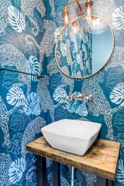 ELMHURST, IL, ABD - 28 Haziran 2020: Mavi duvar kağıdıyla güzel bir yarım banyo, Edison ampulleri, altın yuvarlak ayna ve ahşap bir masa üzerindeki lavabo.