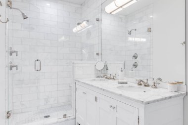 Şikago, IL, ABD - 10 Eylül 2020: Çift kibrli ve bronz musluklu lüks bir beyaz banyo, beyaz bir metro fayanslı duş ve cam kapı.
