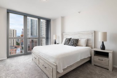 Şikago, IL, ABD - 16 Ağustos 2020 - Şikago şehir merkezine bakan hafif ahşap mobilyaları ve gece lambaları olan parlak, beyaz bir yatak odası.