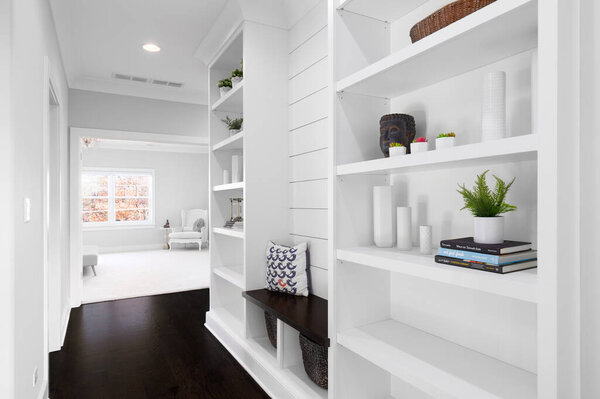 ELMHURST, IL, USA - OCTOBER 20, 2020: A white, built-in shelving in the hallway with shiplap, decorations on the shelves, a wooden bench, and looking towards a bright bedroom.