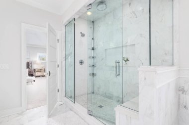 ELMHURST, IL, ABD - 4 Kasım 2020: mermer kiremitler ve cam duvarlar ile büyük lüks bir duş. Banyo büyük, rahat bir yatak odasına bakıyor..