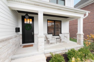 OAK PARK, IL, ABD - 15 Kasım 2020: Pencereleri, beyaz sütunları, taş zemini ve bahçe mobilyaları olan siyah ahşap kapılı yeni, beyaz bir çiftlik evi.