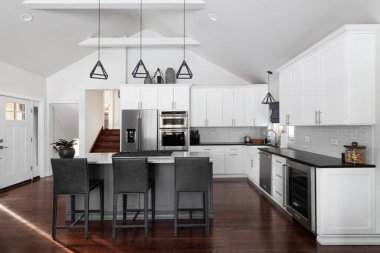 ELMHURST, IL, ABD - 12 HAZİRAN 2021: Modern bir çiftlik evinde güzel beyaz bir mutfak, adanın tavanından sarkan siyah ışıklar, bar tabureleri ve KitchenAid çelik aletleri.